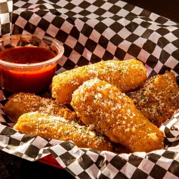Golden-brown mozzarella sticks, sprinkled with parmesan cheese, served with marinara sauce in a checkered basket.