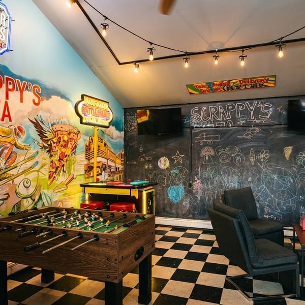 A game room with a foosball table, chalkboard walls, and a colorful mural for Scrappy's Pizza.